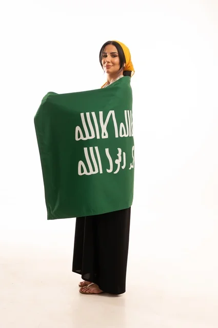 ذكرى تأسيس الدولة السعودية الأولى 22 فبراير، يوم بدينا 1727 م، ارتداء أزياء المنطقة الوسطى، الاحتفال بالمناسبات والأعياد الوطنية الشعبية، بورتريه لامرأة عربية خليجية سعودية مبتسمة ترتدي الكرتة والهامة تضع على كتفيها علم يوم التأسيس، الجسم بالطول الكامل، خلفية بيضاء