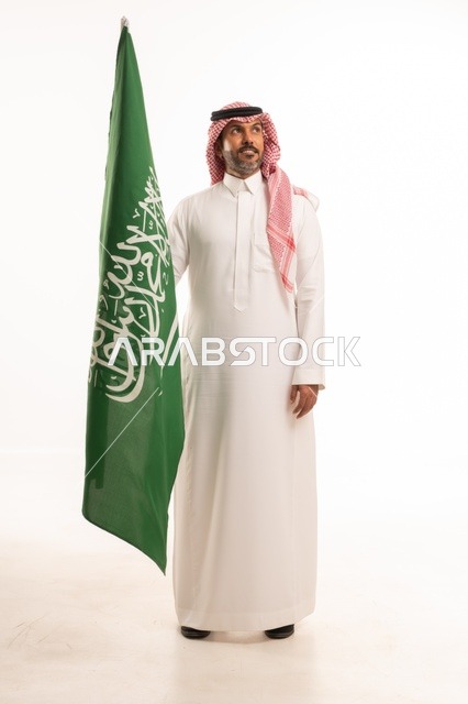 يوم العلم السعودي 11 مارس، إحياء ذكرى اليوم الوطني السعودي 23 سبتمبر, إيماءات الفخر و السرور بالانتماء للوطن, بورتريه لرجل عربي خليجي سعودي مبتسم يرتدي الشماغ و الثوب التقليدي يحمل بيده علم المملكة، يوم بدينا 1727 م، الجسم بالطول الكامل، خلفية بيضاء