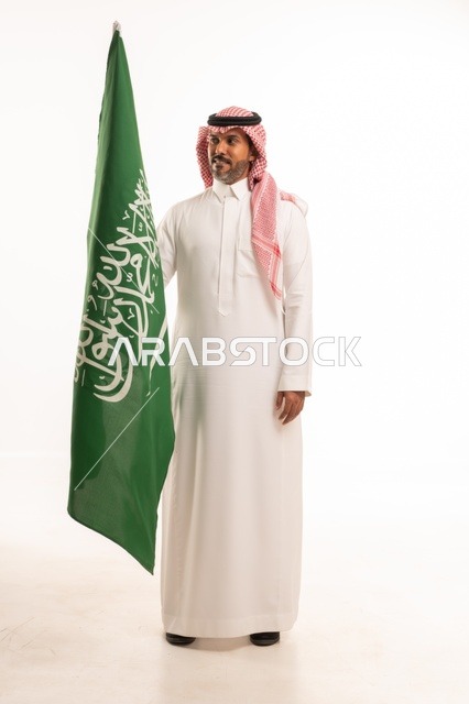 يوم العلم السعودي 11 مارس، إحياء ذكرى اليوم الوطني السعودي 23 سبتمبر, إيماءات الفخر و السرور بالانتماء للوطن, بورتريه لرجل عربي خليجي سعودي مبتسم يرتدي الشماغ و الثوب التقليدي يحمل بيده علم المملكة، يوم بدينا 1727 م، الجسم بالطول الكامل، خلفية بيضاء