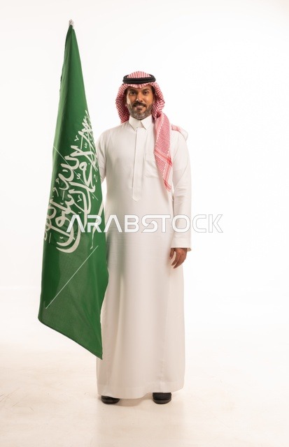 يوم العلم السعودي 11 مارس، إحياء ذكرى اليوم الوطني السعودي 23 سبتمبر, إيماءات الفخر و السرور بالانتماء للوطن, بورتريه لرجل عربي خليجي سعودي مبتسم يرتدي الشماغ و الثوب التقليدي يحمل بيده علم المملكة، يوم بدينا 1727 م، الجسم بالطول الكامل، خلفية بيضاء