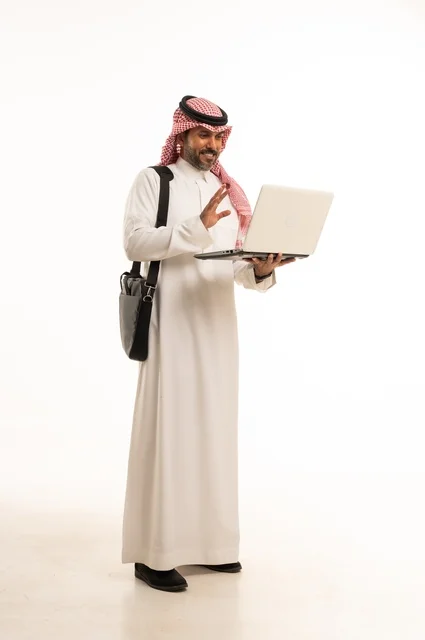 Chatting and conversations and social communication, conducting a business meeting online, completing remote work tasks, online shopping and online orders, a portrait of an Arab Saudi Gulf man wearing traditional thobe and ghutrah, carrying a briefcase and using a laptop, full body, white background.