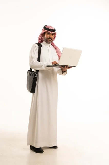 Chatting and conversations and social communication, conducting a business meeting online, completing remote work tasks, online shopping and online orders, a portrait of an Arab Saudi Gulf man wearing traditional thobe and ghutrah, carrying a briefcase and using a laptop, full body, white background.