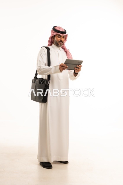 Completing remote work tasks, online shopping and orders, chatting and social communication, conducting a business meeting online, a portrait of an Arab Saudi Gulf man wearing traditional thobe and ghutrah, carrying a briefcase and using a tablet, full-body, white background.