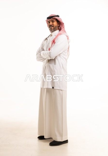 تعابير يد تشابك يدين النظر إلى الكاميرا بايماءات الثقة بالنفس، الاهتمام بالمظهر الخارجي، تقديم الفحص الطبي والخدمات العلاجية، بورتريه مقرب لطبيب عربي خليجي سعودي مبتسم يرتدي معطف الطبيب ويضع السماعات الطبية، مفهوم الرعاية الصحية، خلفية بيضاء