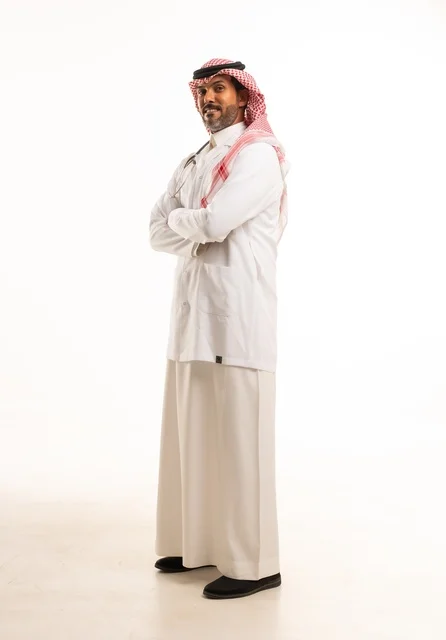 تعابير يد تشابك يدين النظر إلى الكاميرا بايماءات الثقة بالنفس، الاهتمام بالمظهر الخارجي، تقديم الفحص الطبي والخدمات العلاجية، بورتريه مقرب لطبيب عربي خليجي سعودي مبتسم يرتدي معطف الطبيب ويضع السماعات الطبية، مفهوم الرعاية الصحية، خلفية بيضاء