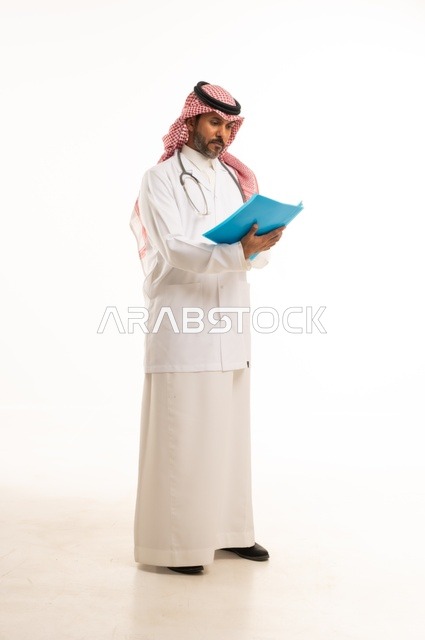 متابعة حالات المرضى والتوصيات اللازمة لكل مريض، بورتريه لطبيب عربي خليجي سعودي يرتدي الثوب التقليدي والمئزر الأبيض يمسك بيديه ملفات المرضى، شاب سعودي ينظر إلى الكاميرا بتعابير الحزم والجدية, خلفية بيضاء