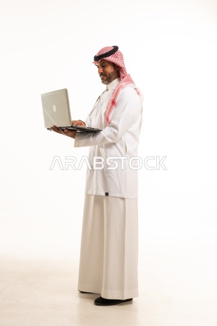 دمج التكنولوجيا مع الحياة العملية، الاهتمام بالمظهر الخارجي،  تقديم الفحص الطبي والخدمات العلاجية، بورتريه مقرب لطبيب عربي خليجي سعودي مبتسم يرتدي معطف الطبيب ويضع السماعات الطبية يحمل بيده حاب محمول يستخدمه لمراجعة حالات المرضى، الرعاية الصحية، خلفية بيضاء