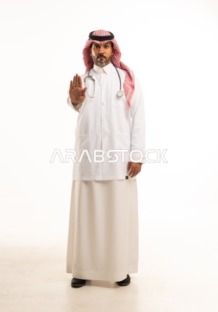 تعابير يد قف النظر إلى الكاميرا بايماءات الثقة بالنفس، الاهتمام بالمظهر الخارجي، تقديم الفحص الطبي والخدمات العلاجية، بورتريه مقرب لطبيب عربي خليجي سعودي مبتسم يرتدي معطف الطبيب ويضع السماعات الطبية، مفهوم الرعاية الصحية، خلفية بيضاء