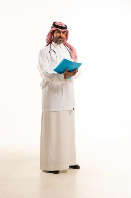 متابعة حالات المرضى والتوصيات اللازمة لكل مريض، بورتريه لطبيب عربي خليجي سعودي يرتدي الثوب التقليدي والمئزر الأبيض يمسك بيديه ملفات المرضى، شاب سعودي ينظر إلى الكاميرا بتعابير الحزم والجدية, خلفية بيضاء