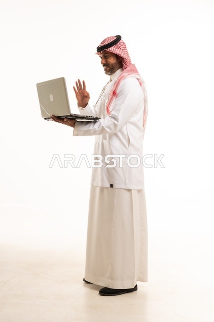 Video call via a communication app, attention to appearance, providing medical examinations and treatment services, a close-up portrait of a smiling Arab Gulf Saudi doctor wearing a lab coat and stethoscope, holding a mobile phone in his hand to review patient cases, healthcare, white background.