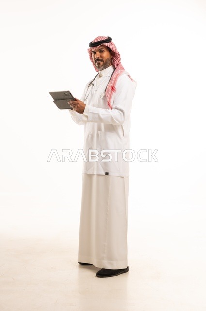 Integrating technological advancement into practical life, paying attention to external appearance, providing medical examinations and treatment services, a close-up portrait of a smiling Arab Gulf Saudi doctor wearing a doctor's coat and stethoscope, holding a tablet in his hand used to review patient cases, healthcare, white background.