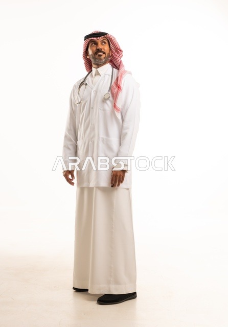 يدين إلى الجانب النظر إلى الكاميرا بايماءات الثقة بالنفس، الاهتمام بالمظهر الخارجي، تقديم الفحص الطبي والخدمات العلاجية، بورتريه مقرب لطبيب عربي خليجي سعودي مبتسم يرتدي معطف الطبيب ويضع السماعات الطبية، مفهوم الرعاية الصحية، خلفية بيضاء