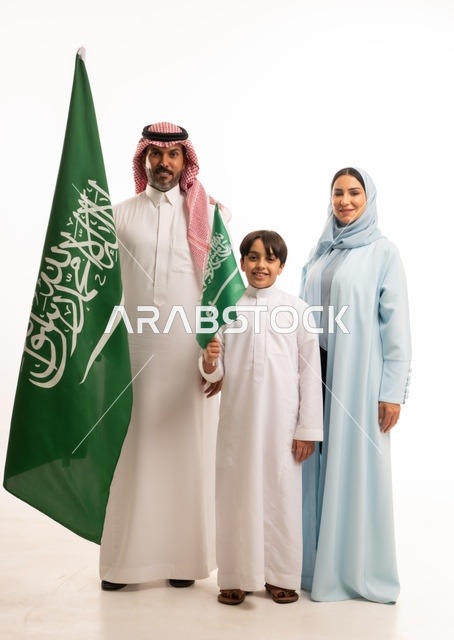 الأجواء العائلية المليئة بالحب، بورتريه لعائلة عربية خليجية سعودية سعيدة تمسك بعلم السعودية بحب وفخر، الاحتفال بيوم العلم 11 مارس، العيد الوطني السعودي 8 ربيع الأول، ذكرى اليوم الوطني السعودي، الأعياد والمناسبات الوطنية السعودية، خلفية بيضاء
