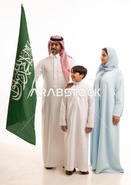 الأجواء العائلية المليئة بالحب، بورتريه لعائلة عربية خليجية سعودية سعيدة تمسك بعلم السعودية بحب وفخر، الاحتفال بيوم العلم 11 مارس، العيد الوطني السعودي 8 ربيع الأول، ذكرى اليوم الوطني السعودي، الأعياد والمناسبات الوطنية السعودية، خلفية بيضاء
