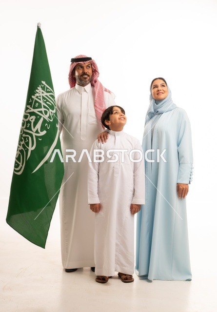الأجواء العائلية المليئة بالحب، بورتريه لعائلة عربية خليجية سعودية سعيدة تمسك بعلم السعودية بحب وفخر، الاحتفال بيوم العلم 11 مارس، العيد الوطني السعودي 8 ربيع الأول، ذكرى اليوم الوطني السعودي، الأعياد والمناسبات الوطنية السعودية، خلفية بيضاء