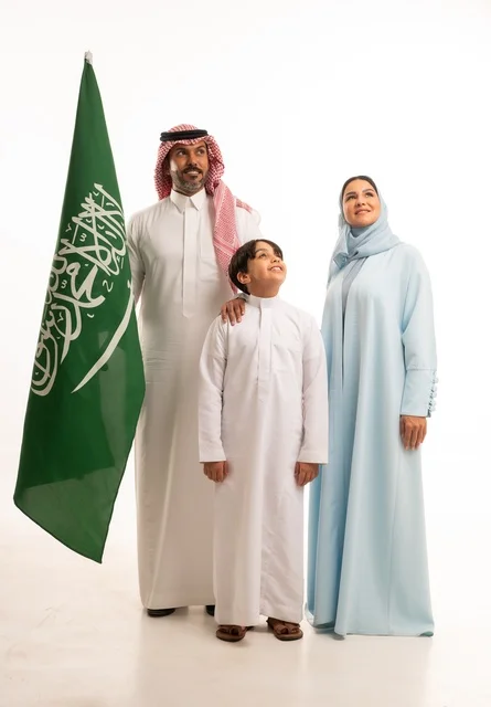 الأجواء العائلية المليئة بالحب، بورتريه لعائلة عربية خليجية سعودية سعيدة تمسك بعلم السعودية بحب وفخر، الاحتفال بيوم العلم 11 مارس، العيد الوطني السعودي 8 ربيع الأول، ذكرى اليوم الوطني السعودي، الأعياد والمناسبات الوطنية السعودية، خلفية بيضاء