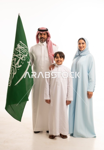 الأجواء العائلية المليئة بالحب، بورتريه لعائلة عربية خليجية سعودية سعيدة تمسك بعلم السعودية بحب وفخر، الاحتفال بيوم العلم 11 مارس، العيد الوطني السعودي 8 ربيع الأول، ذكرى اليوم الوطني السعودي، الأعياد والمناسبات الوطنية السعودية، خلفية بيضاء
