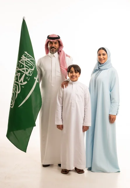 الأجواء العائلية المليئة بالحب، بورتريه لعائلة عربية خليجية سعودية سعيدة تمسك بعلم السعودية بحب وفخر، الاحتفال بيوم العلم 11 مارس، العيد الوطني السعودي 8 ربيع الأول، ذكرى اليوم الوطني السعودي، الأعياد والمناسبات الوطنية السعودية، خلفية بيضاء