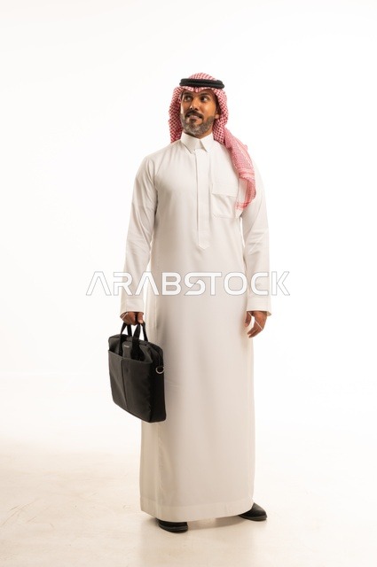 مفهوم إداة الأعمال والمشاريع، الاستعداد للذهاب إلى العمل، بورتريه لرجل عربي خليجي سعودي يرتدي الثوب التقليدي والشماغ يحمل بيده حقيبة يد يقف باستقامة بإيماءات الثقة بالنفس، الأناقة والاهتمام بالمظهر الخارجي، الجسم بالطول الكامل، خلفيه بيضاء