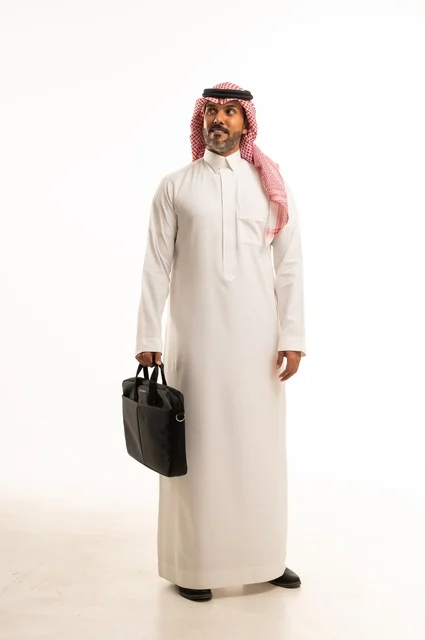 مفهوم إداة الأعمال والمشاريع، الاستعداد للذهاب إلى العمل، بورتريه لرجل عربي خليجي سعودي يرتدي الثوب التقليدي والشماغ يحمل بيده حقيبة يد يقف باستقامة بإيماءات الثقة بالنفس، الأناقة والاهتمام بالمظهر الخارجي، الجسم بالطول الكامل، خلفيه بيضاء