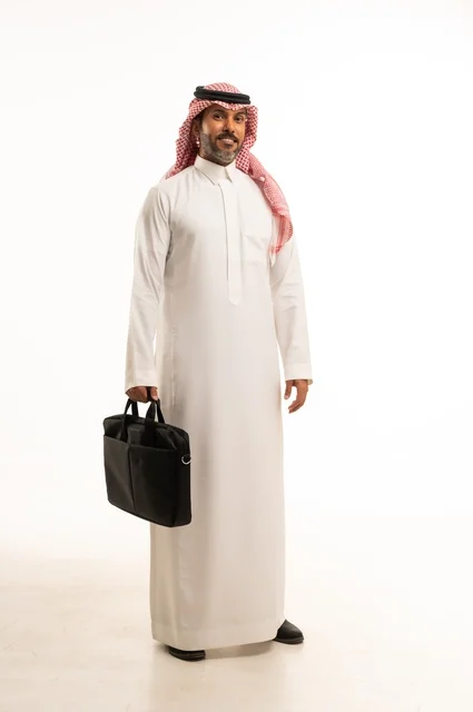 The concept of business and project management, readiness to go to work, a portrait of an Arab Gulf Saudi man wearing traditional attire and a shemagh, holding a handbag, standing upright with gestures of self-confidence, elegance, and attention to appearance, full-body, white background.