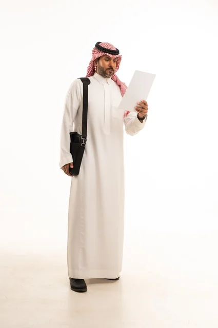 قراءة وتدقيق الملاحظات، مفهوم إداة الأعمال والمشاريع، الاستعداد للذهاب إلى العمل، بورتريه لرجل عربي خليجي سعودي يرتدي الثوب التقليدي والشماغ يحمل بيده حقيبة يد وورقة بيضاء، الأناقة والاهتمام بالمظهر الخارجي، الجسم بالطول الكامل، خلفيه بيضاء