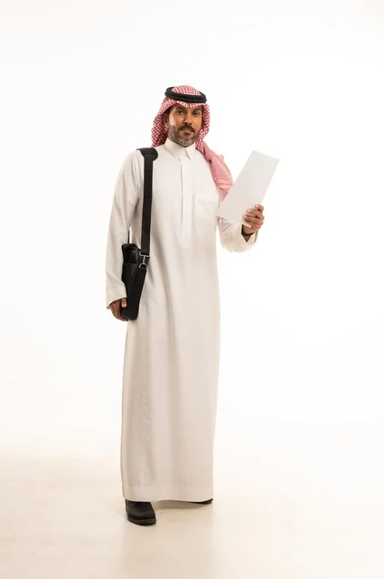 قراءة وتدقيق الملاحظات، مفهوم إداة الأعمال والمشاريع، الاستعداد للذهاب إلى العمل، بورتريه لرجل عربي خليجي سعودي يرتدي الثوب التقليدي والشماغ يحمل بيده حقيبة يد وورقة بيضاء، الأناقة والاهتمام بالمظهر الخارجي، الجسم بالطول الكامل، خلفيه بيضاء