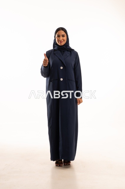 أشارة باستخدام اصبع الأبهام للأعلى تعابير وجه ابتسامة، الاهتمام بالمظهر الخارجي والأناقة، تعابير السرور والسعادة، بورتريه لإمرأة عربية خليجية سعودية محجبة ترتدي عباءة، شابة سعودية ، صورة الجسم بالطول الكامل، خلفية بيضاء