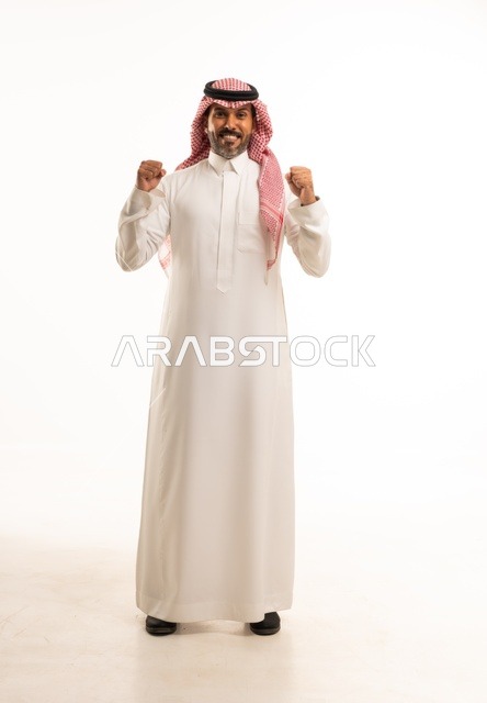 الفوز وتحقيق الأهداف، زيادة قدرة العضلات على التحمل، إتقان فنون الملاكمة، بورتريه لرجل عربي خليجي سعودي يرتدي الزي التقليدي يرفع قبضات يديه بإيماءات القوة، النظر إلى الكاميرا بتعابير الثقة بالنفس، ممارسة رياضة الدفاع عن النفس، الجسم بالطول الكامل، خلفية بيضاء