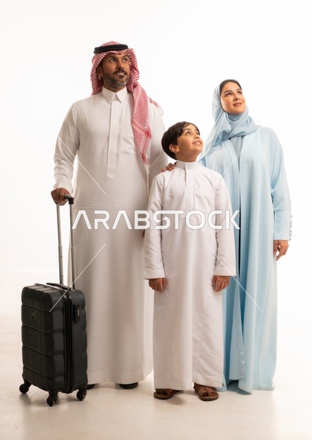 تجهيز حقيبة السفر، أنشطة سياحية ترفيهية، التأهب لرحلة سفر و قضاء اوقات ممتعة في العطلة مع الاهل، بورتريه لزوجان عربيان خليجيان سعوديان يقفان مع ابنهما بإيماءات السعادة والسرور، المحافظة على تماسك الأسرة، الجسم بالطول الكامل، خلفية بيضاء
