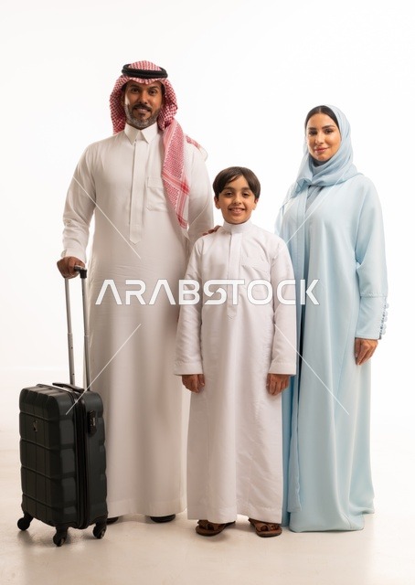 تجهيز حقيبة السفر، أنشطة سياحية ترفيهية، التأهب لرحلة سفر و قضاء اوقات ممتعة في العطلة مع الاهل، بورتريه لزوجان عربيان خليجيان سعوديان يقفان مع ابنهما بإيماءات السعادة والسرور، المحافظة على تماسك الأسرة، الجسم بالطول الكامل، خلفية بيضاء