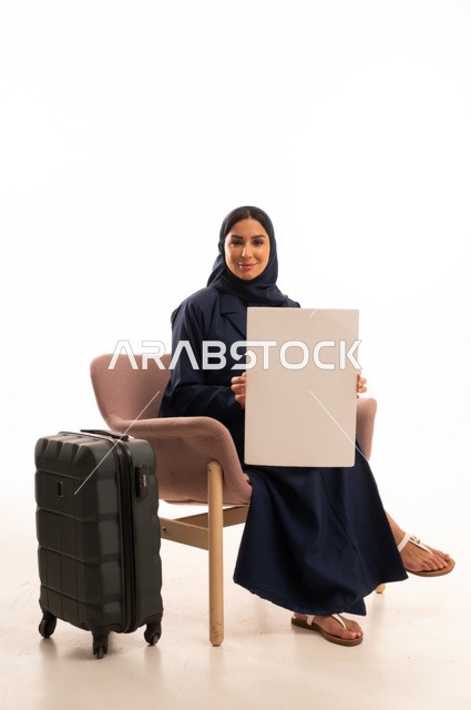 موك أب مستطيل أبيض، العروض والإعلانات التسويقية، الاهتمام بالمظهر الخارجي والأناقة، بورتريه لإمرأة عربية خليجية سعودية محجبة ترتدي عباءة تجلس على كرسي وردي وبجانبها حقيبة سفر سوداء، شابة سعودية ، خلفية بيضاء
