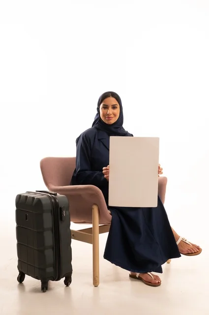 موك أب مستطيل أبيض، العروض والإعلانات التسويقية، الاهتمام بالمظهر الخارجي والأناقة، بورتريه لإمرأة عربية خليجية سعودية محجبة ترتدي عباءة تجلس على كرسي وردي وبجانبها حقيبة سفر سوداء، شابة سعودية ، خلفية بيضاء