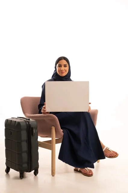 موك أب مستطيل أبيض، العروض والإعلانات التسويقية، الاهتمام بالمظهر الخارجي والأناقة، بورتريه لإمرأة عربية خليجية سعودية محجبة ترتدي عباءة تجلس على كرسي وردي وبجانبها حقيبة سفر سوداء، شابة سعودية ، خلفية بيضاء