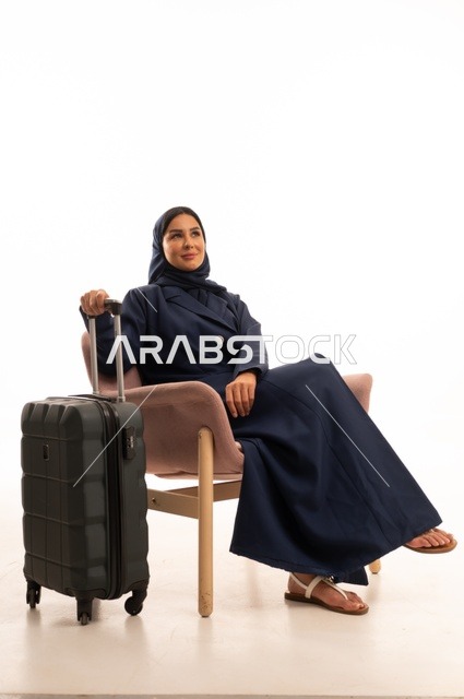 النظر إلى الأعلى بإيماءات التمني والتأمل، الاهتمام بالمظهر الخارجي والأناقة، بورتريه لإمرأة عربية خليجية سعودية محجبة ترتدي عباءة تجلس على كرسي وردي وتمسك بيدها حقيبة سفر سوداء، شابة سعودية ، خلفية بيضاء
