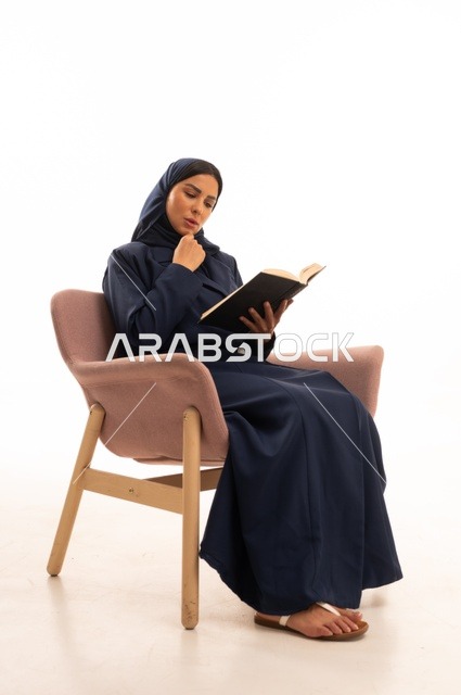 تعابير الاندماج والتركيز، المطالعة والقراءة اكتساب معلومات ثقافية جديدة،الاهتمام بالمظهر الخارجي والأناقة، بورتريه لإمرأة عربية خليجية سعودية محجبة ترتدي عباءة تجلس على كرسي وردي تمسك بيدها كتاب، شابة سعودية ، خلفية بيضاء