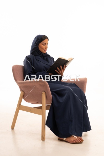 تعابير الاندماج والتركيز، المطالعة والقراءة اكتساب معلومات ثقافية جديدة،الاهتمام بالمظهر الخارجي والأناقة، بورتريه لإمرأة عربية خليجية سعودية محجبة ترتدي عباءة تجلس على كرسي وردي تمسك بيدها كتاب، شابة سعودية ، خلفية بيضاء