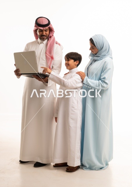 متابعة حصص الأونلاين وإجراء مكالمة فيديو من خلال الحاسوب المحمول، بورتريه لرجل عربي سعودي خليجي يحمل اللابتوب ويقف برفقة زوجته وابنه، الأجواء العائلية المليئة بالحب والترابط والإستقرار، الجسم بالطول الكامل، خلفية بيضاء