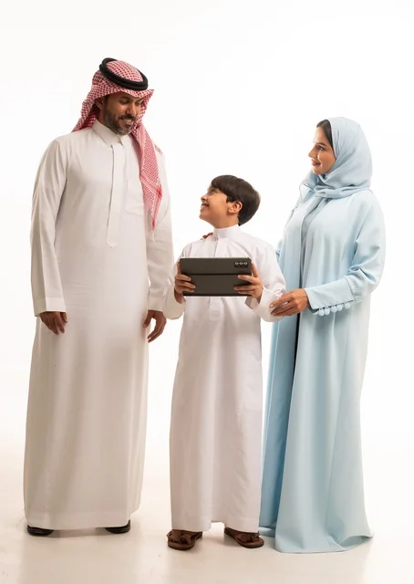 استخدام جهاز تقني حديث، متابعة حصص الأونلاين وإجراء مكالمة فيديو من خلال الجهاز اللوحي، بورتريه لرجل عربي سعودي خليجي يرتدي الثوب التقليدي يحمل التابليت ويقف برفقة والديه، الأجواء العائلية المليئة بالحب والترابط والإستقرار، الجسم بالطول الكامل، خلفية بيضاء