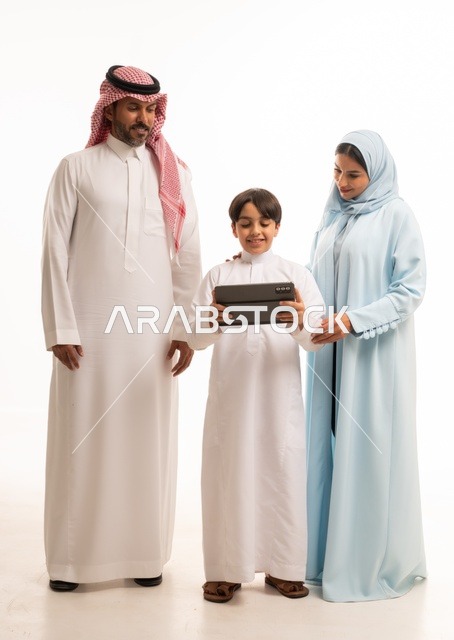 استخدام جهاز تقني حديث، متابعة حصص الأونلاين وإجراء مكالمة فيديو من خلال الجهاز اللوحي، بورتريه لرجل عربي سعودي خليجي يرتدي الثوب التقليدي يحمل التابليت ويقف برفقة والديه، الأجواء العائلية المليئة بالحب والترابط والإستقرار، الجسم بالطول الكامل، خلفية بيضاء