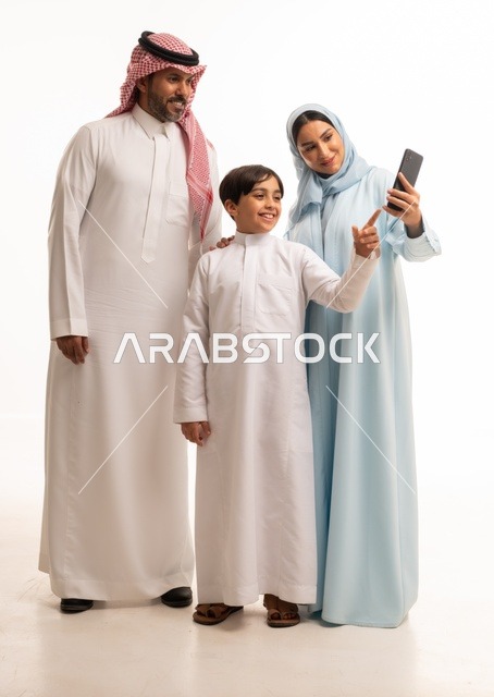 الاجتماع الأسري وبناء مجتمع سعودي متنامي, التقاط سيلفي عائلي تذكاري عبر الهاتف المحمول, بورتريه لعائلة عربية سعودية خليجية مبتسمة تقوم بتوثيق اللحظات الممتعة بإيماءات السعادة والفرح, فرحة الأبناء بقضاء وقت ممتع مع الأهل, خلفية بيضاء