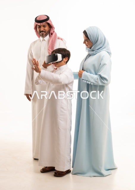 الاستمتاع بمشاهدة الأفلام ومحاكاة العالم الإفتراضي، بورتريه لولد عربي سعودي خليجي برفقة والديه يرتدي نظارات الواقع الإفتراضي (في آر) ثلاثية الإبعاد، مفهوم الإهتمام والإعتناء بالأبناء، أنشطة تقنية ترفيهية مسلية، صورة الجسم بالطول الكامل، خلفية بيضاء