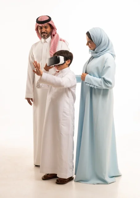 Enjoying watching movies and simulating the virtual world, a portrait of an Arab Saudi Gulf boy with his parents wearing three-dimensional virtual reality (VR) glasses, the concept of caring for and nurturing children, entertaining technological activities, full-body image, white background.