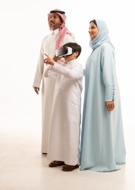 الاستمتاع بمشاهدة الأفلام ومحاكاة العالم الإفتراضي، بورتريه لولد عربي سعودي خليجي برفقة والديه يرتدي نظارات الواقع الإفتراضي (في آر) ثلاثية الإبعاد، مفهوم الإهتمام والإعتناء بالأبناء، أنشطة تقنية ترفيهية مسلية، صورة الجسم بالطول الكامل، خلفية بيضاء