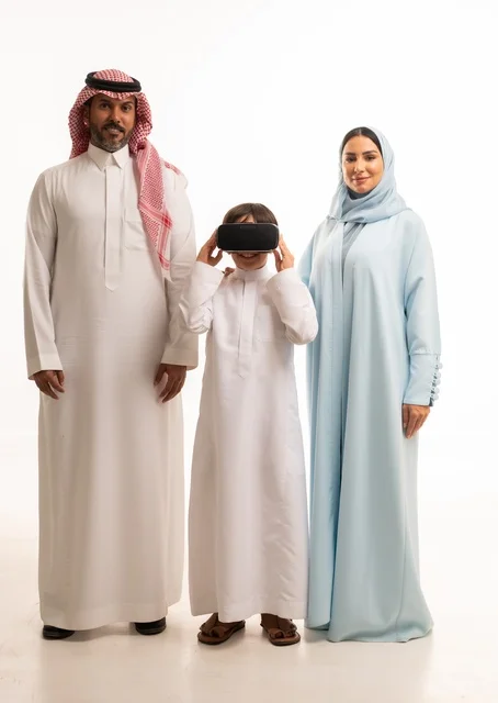 Enjoying watching movies and simulating the virtual world, a portrait of an Arab Saudi Gulf boy with his parents wearing three-dimensional virtual reality (VR) glasses, the concept of caring for and nurturing children, entertaining technological activities, full-body image, white background.