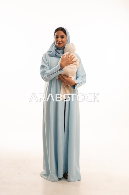 تقوية رابط الأمومة بين الأم وطفلها، مفهوم البراءة والطفولة، تحمل المسؤولية والعناية بالأطفال،  بورتريه لإمرأة عربية خليجية سعودية محجبة تحمل صغيرها بإيماءات الحب والحنان, الجسم بالطول الكامل، خلفية بيضاء