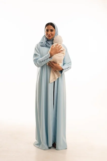 Strengthening the maternal bond between the mother and her child, the concept of innocence and childhood, taking responsibility and caring for children, a portrait of a Saudi Gulf Arab woman in a hijab holding her little one with gestures of love and tenderness, full-body, white background.