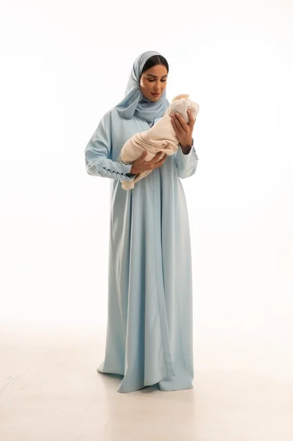 Strengthening the maternal bond between the mother and her child, the concept of innocence and childhood, taking responsibility and caring for children, a portrait of a Saudi Gulf Arab woman in a hijab holding her little one with gestures of love and tenderness, full-body, white background.