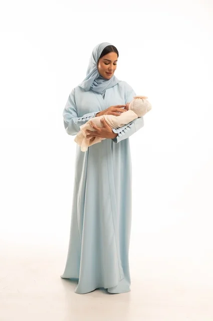 Strengthening the maternal bond between the mother and her child, the concept of innocence and childhood, taking responsibility and caring for children, a portrait of a Saudi Gulf Arab woman in a hijab holding her little one with gestures of love and tenderness, full-body, white background.