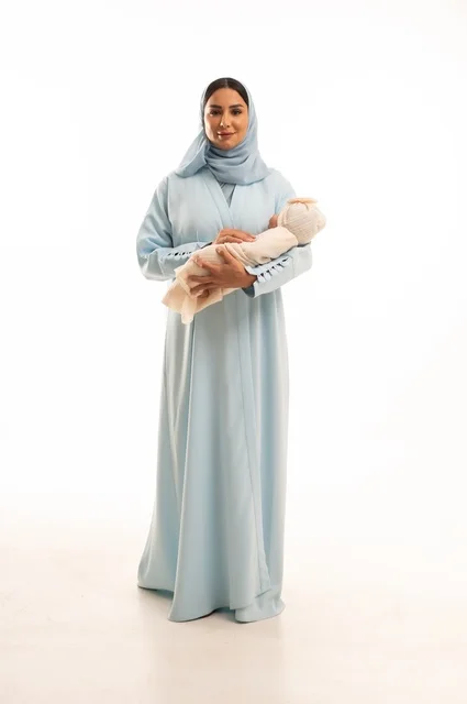 تقوية رابط الأمومة بين الأم وطفلها، مفهوم البراءة والطفولة، تحمل المسؤولية والعناية بالأطفال،  بورتريه لإمرأة عربية خليجية سعودية محجبة تحمل صغيرها بإيماءات الحب والحنان, الجسم بالطول الكامل، خلفية بيضاء